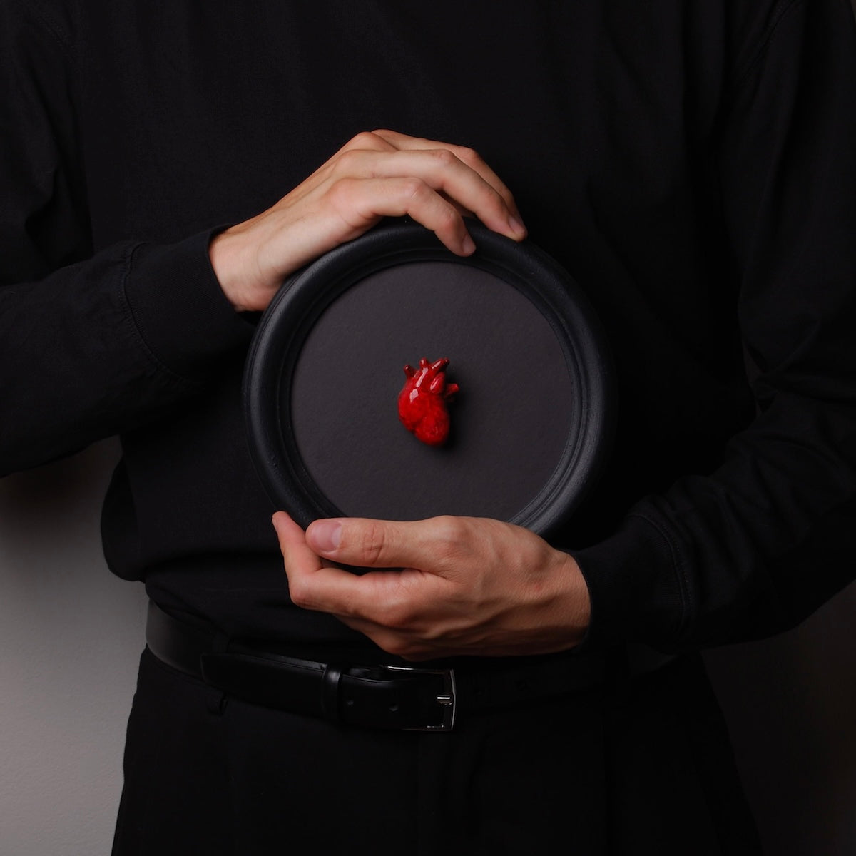 mani che tengono un quadretto rotondo con cornice nera e cuore anatomico rosso