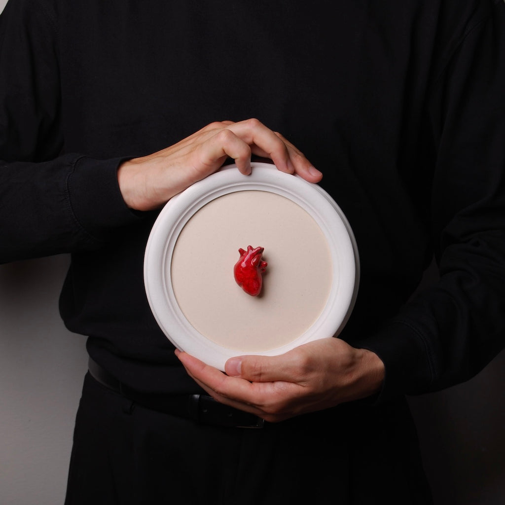 mani che tengono un quadretto rotondo con cornice bianca e cuore anatomico rosso