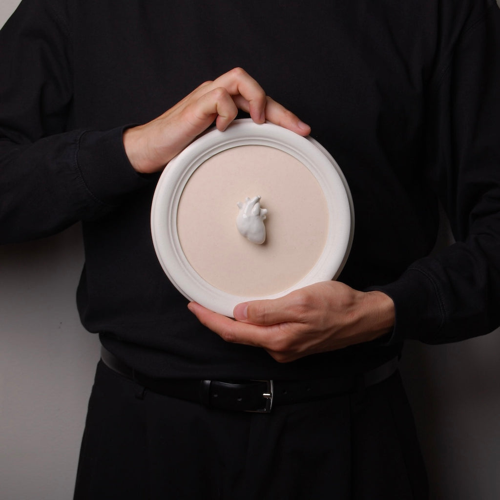 mani che tengono un quadro rotondo con cuore anatomico bianco