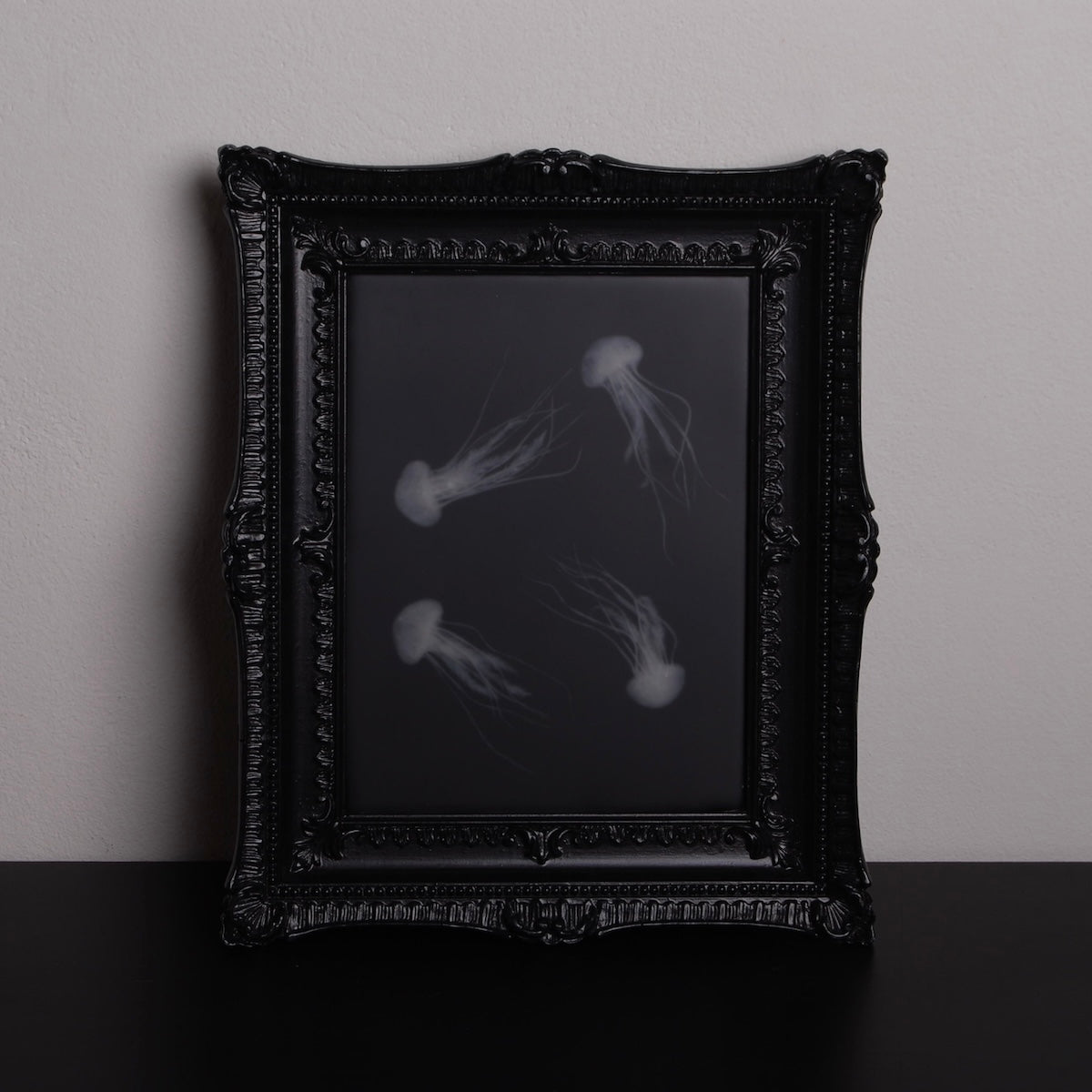 quadro con sculture di meduse marine in cornice rettangolare intarsiata, poggiato in verticale su un piano