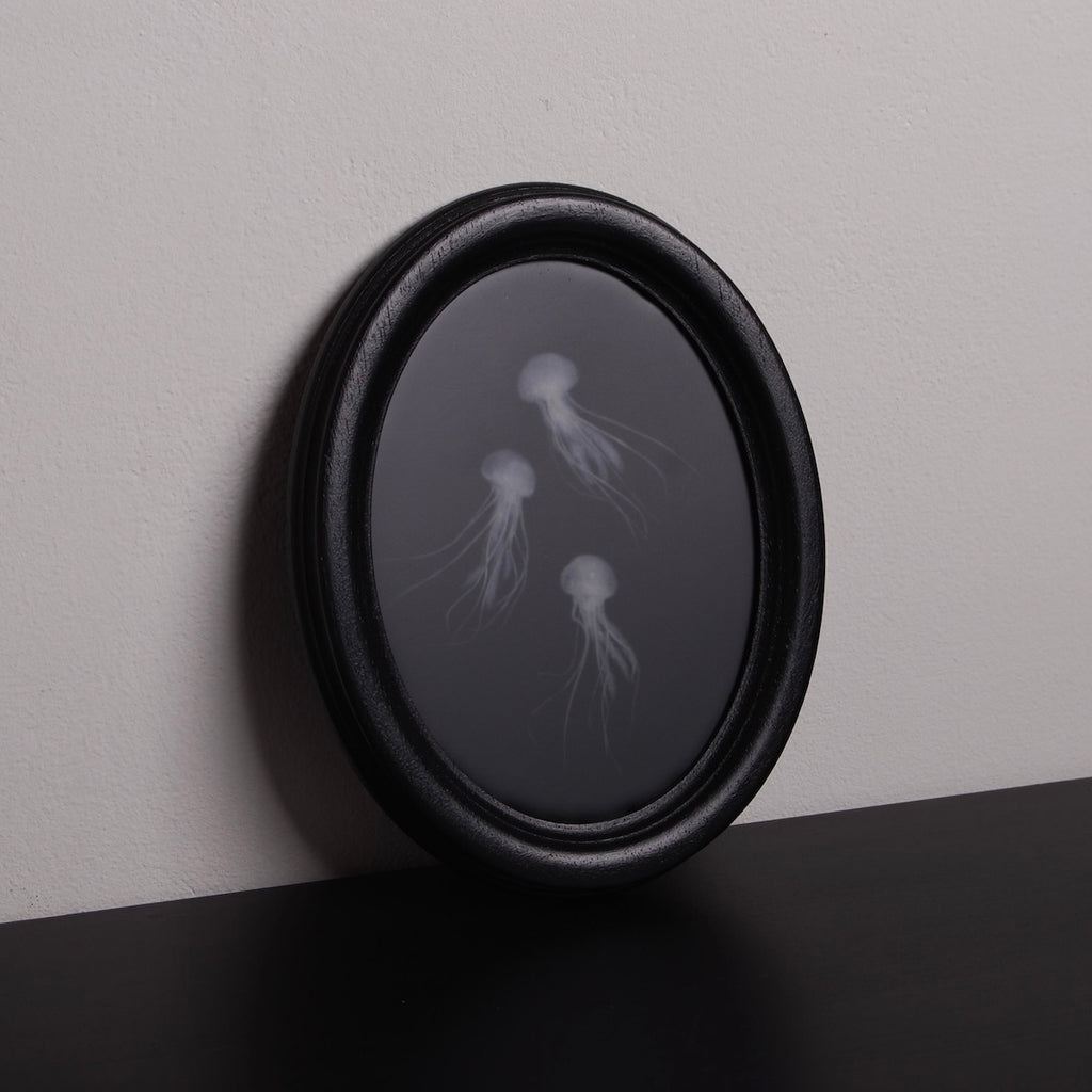 quadro ovale nero con 3 sculture meduse marine poggiato su un ripiano nero
