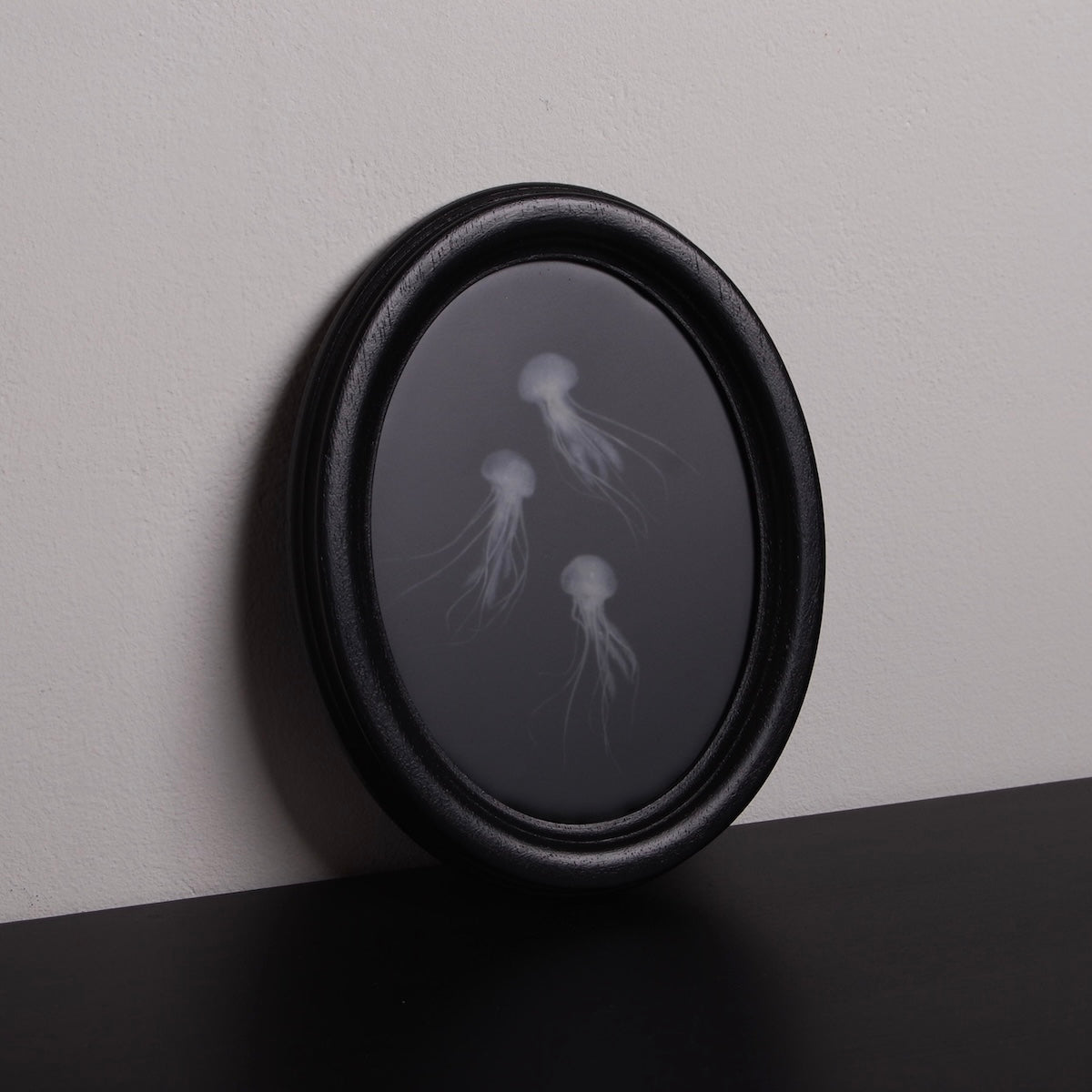 quadro ovale nero con 3 sculture meduse marine poggiato su un ripiano nero
